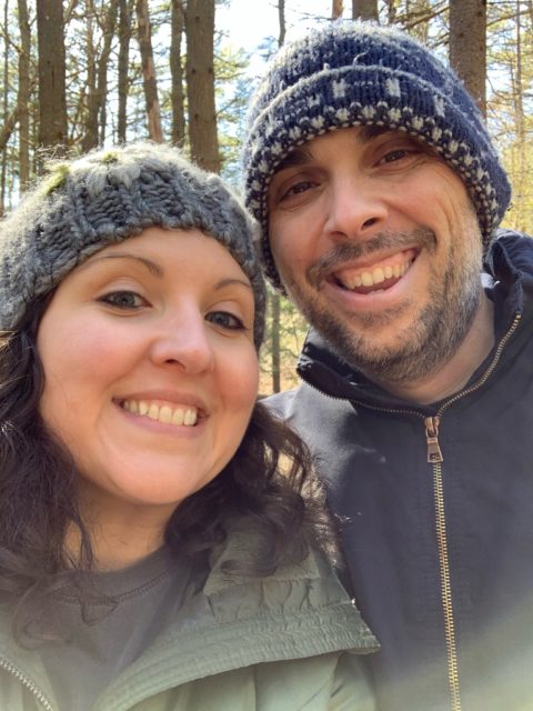 Heidi Clarke and Jason Clarke dressed in hats and coats on a walk in the woods