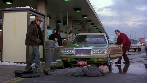 A man opens the driver's side door of a green car with wood paneling on the sides