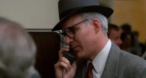 A man dressed in a suit and fedora talks on the phone